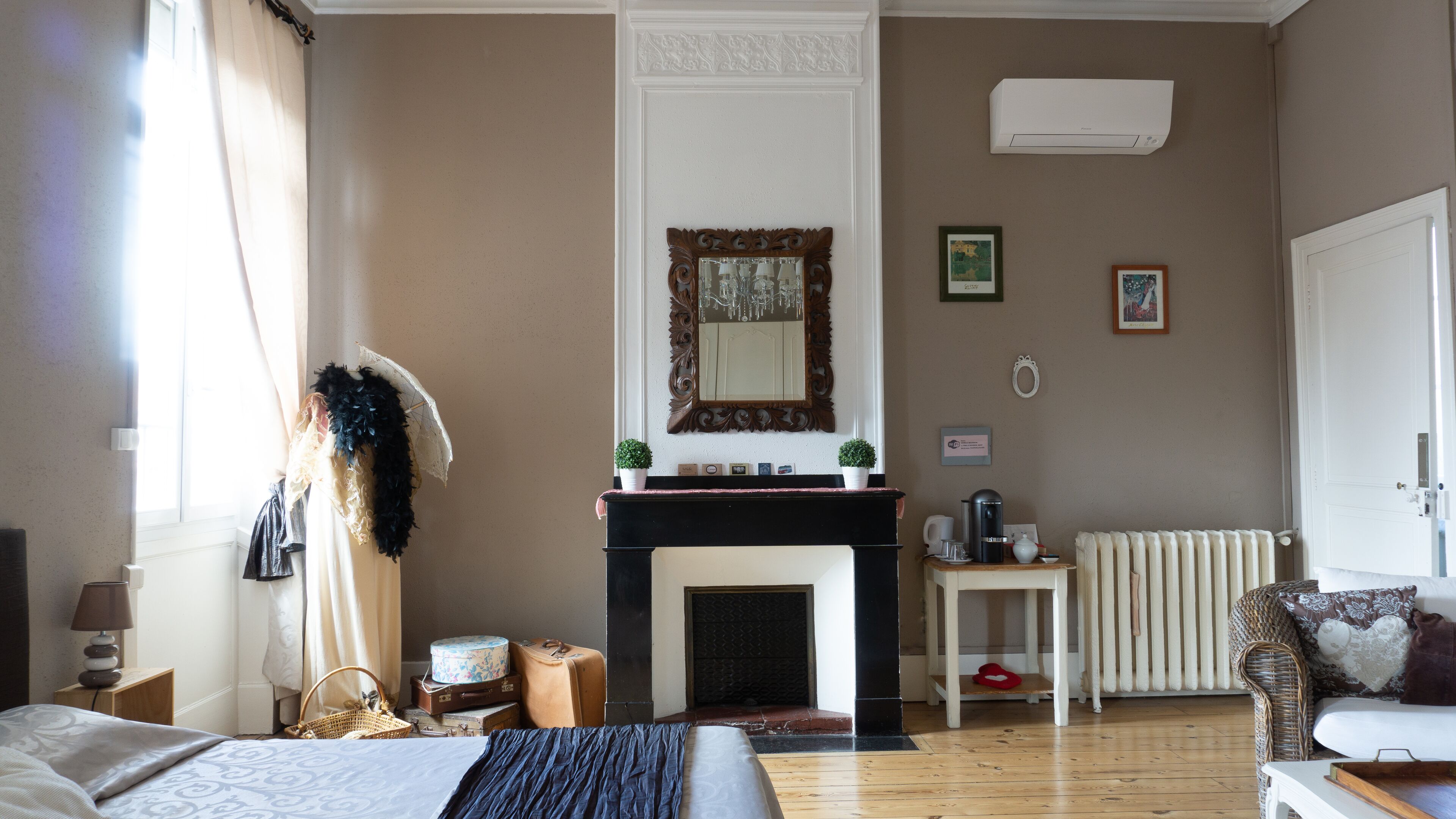 A hotel room with a fireplace, a bed, a small table, a radiator, and a window with curtains.