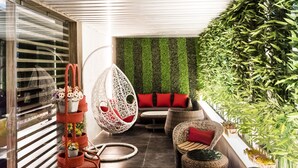 Un área de estar exterior moderna con mobiliario de mimbre, una silla colgante y una pared verde.
