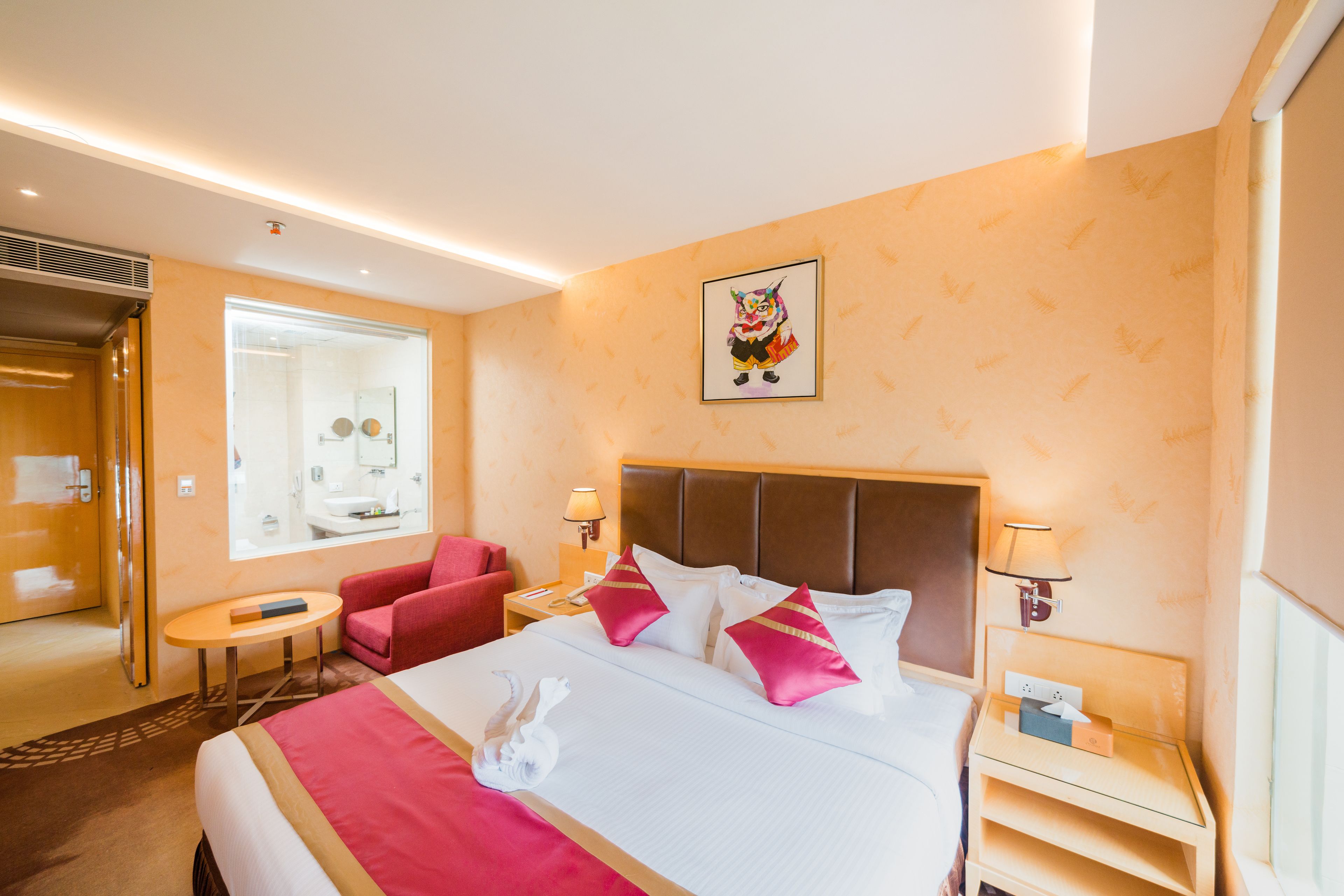 A hotel room with a large bed, a red armchair, a bedside table with a lamp, and a wall-mounted picture.