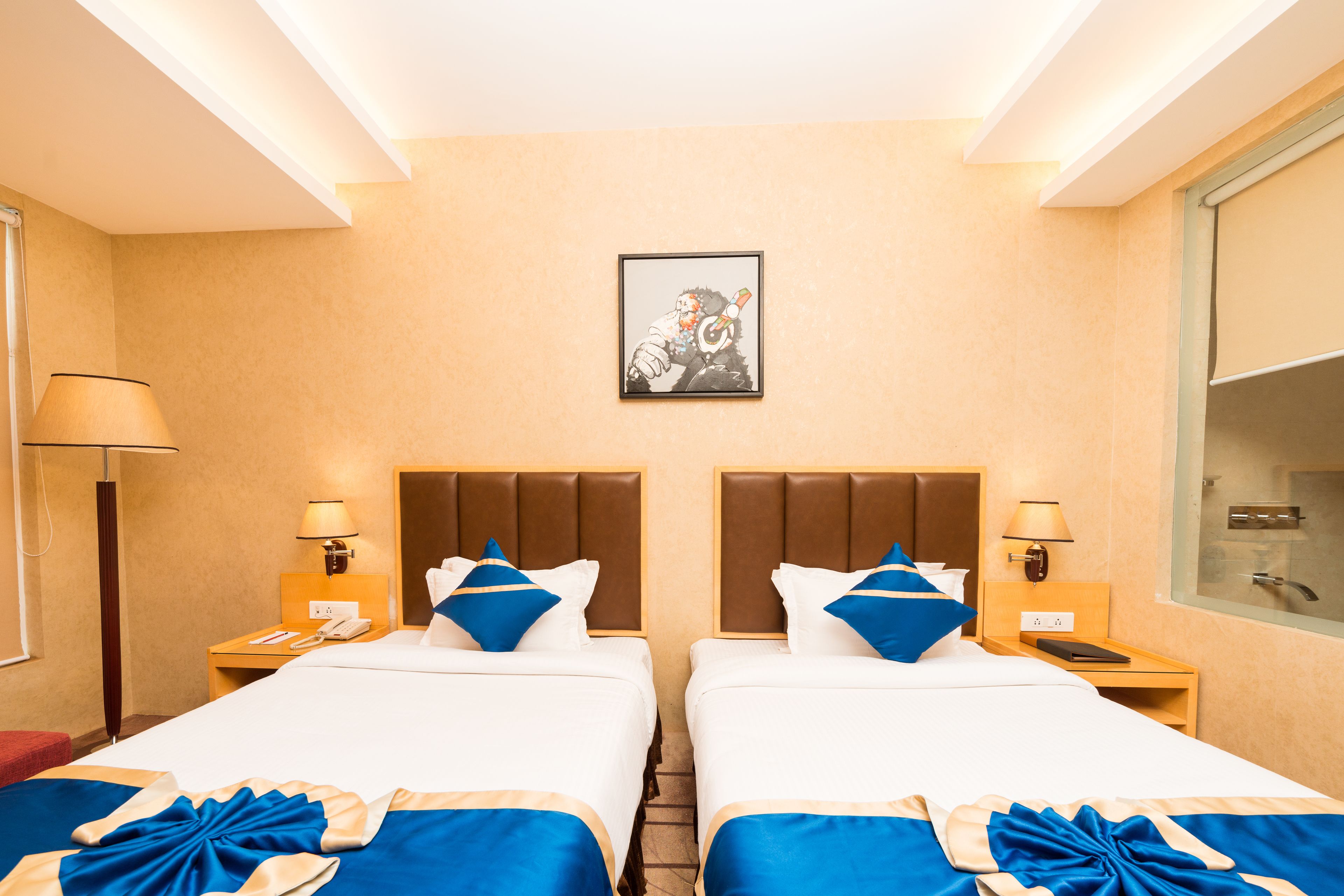 A hotel room with two beds, a framed picture on the wall, and a window with a view.