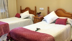 Two double beds with wooden headboards, a nightstand with a vase of flowers, and a wall-mounted light fixture. - Hostal Pachin (Mieres)
