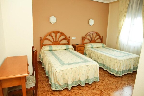 A room with two wooden beds with matching headboards, a wooden table, and a chair.