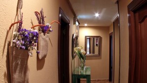 A hallway with a tiled floor, a green table with a vase of flowers, and a mirror on the wall. - Hostal Pachin (Mieres)