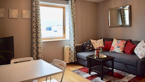 A modern living room with a grey sofa, a dining table with chairs, a coffee table, and a large window with patterned curtains. - Greeg Court (Dublin)