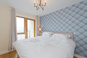 A neatly made bed with white linens, a chandelier, and a plaid-patterned wall.