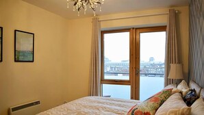 A bedroom with a large bed, a view of a cityscape through a window, and a chandelier. - Greeg Court (Dublin)