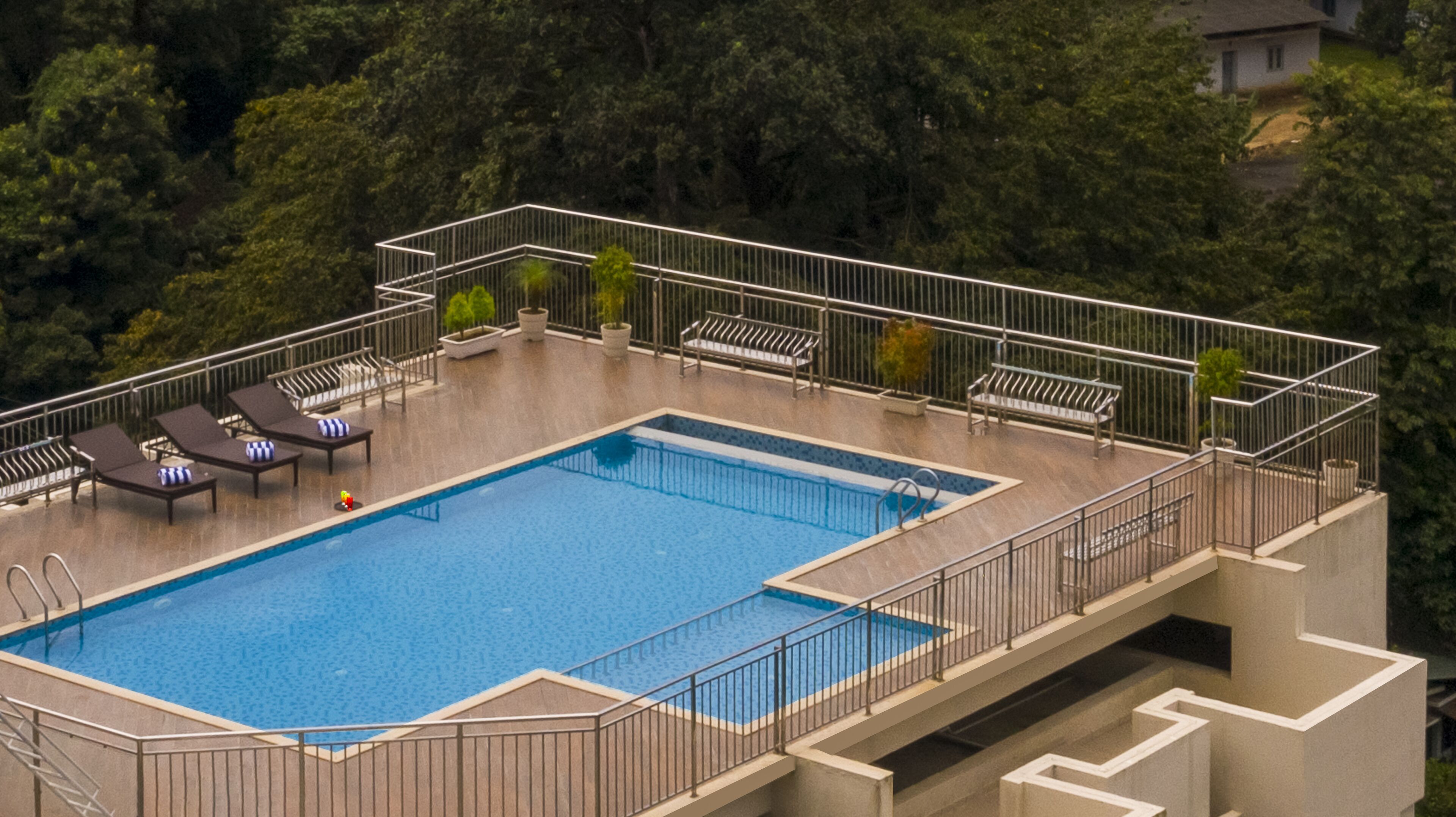 A rooftop pool with lounge chairs, a small pool table, and a view of the surrounding forest.
