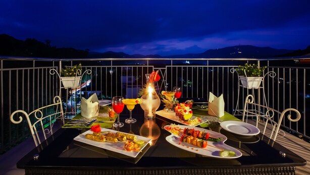 Mesa de comedor lista con diversos platos y bebidas en un balcón con vistas a las montañas de noche.
