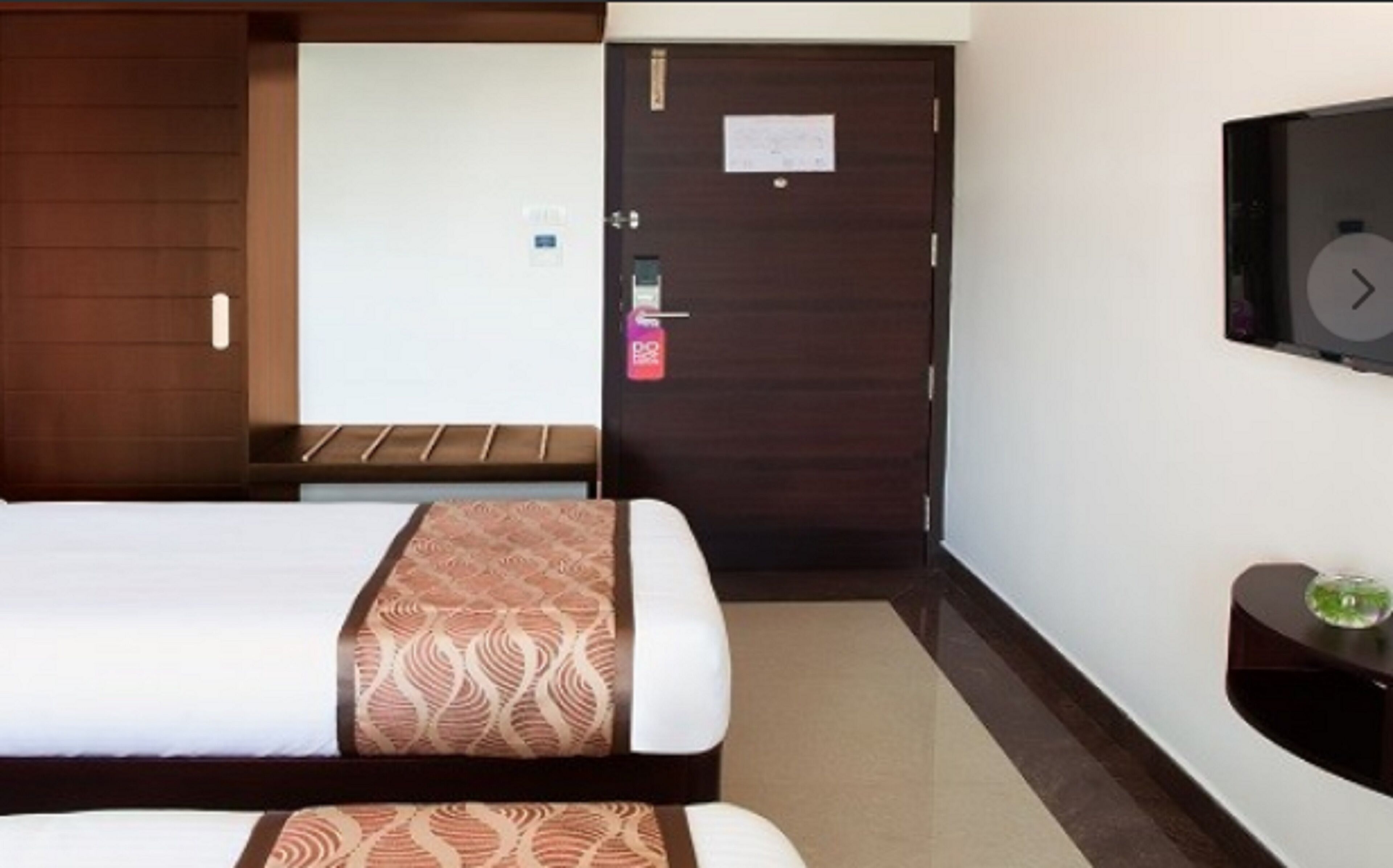 Quarto de hotel com cama, escrivaninha e televisão na parede.