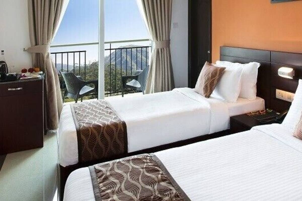 Habitación de hotel con dos camas, televisión, escritorio y balcón con vistas.