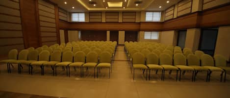 Un salón de conferencias con filas de sillas amarillas, un suelo de mármol pulido y un techo alto con iluminación empotrada.
