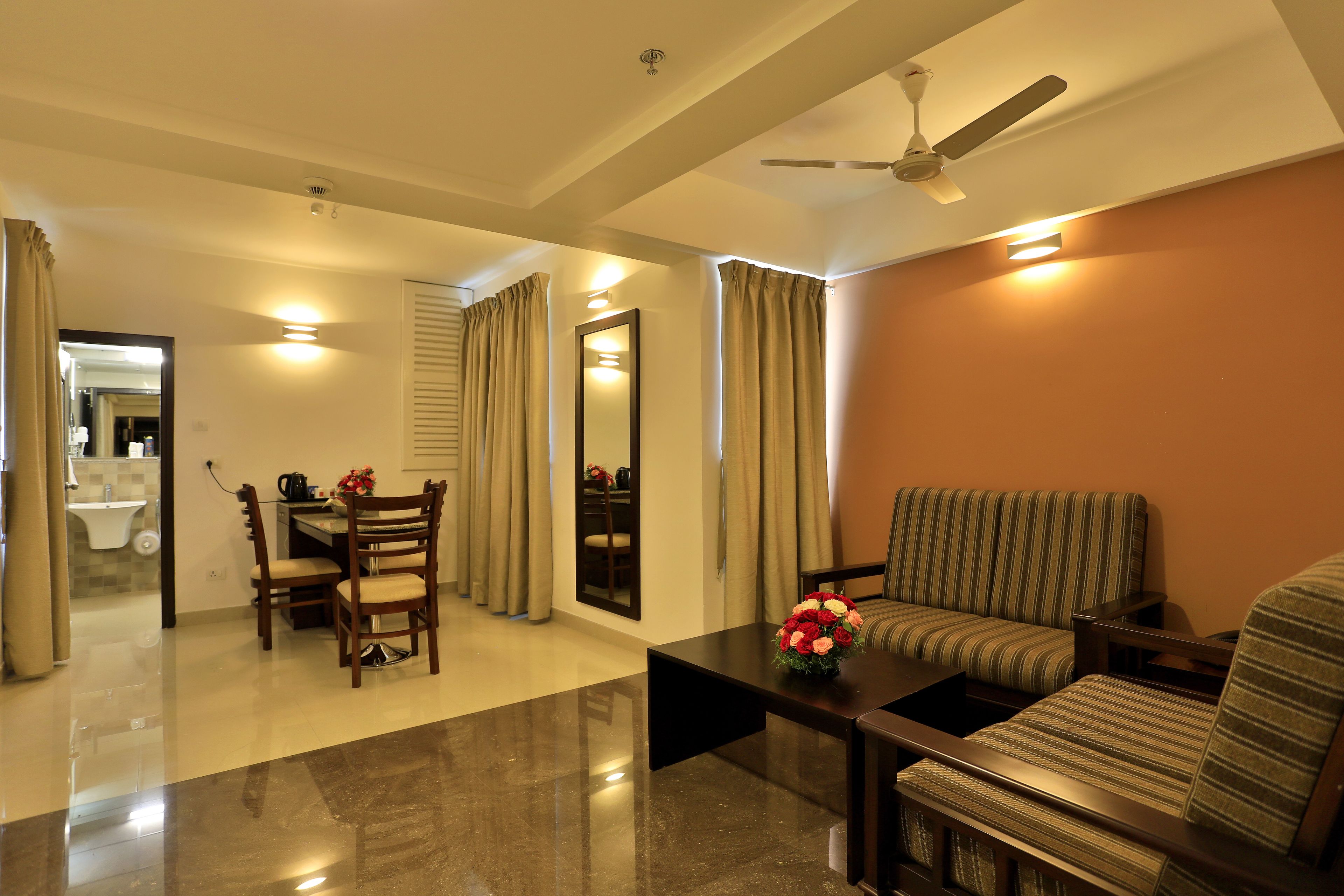A living room with a sofa, a dining table, and chairs. There is a ceiling fan and a mirror on the wall.