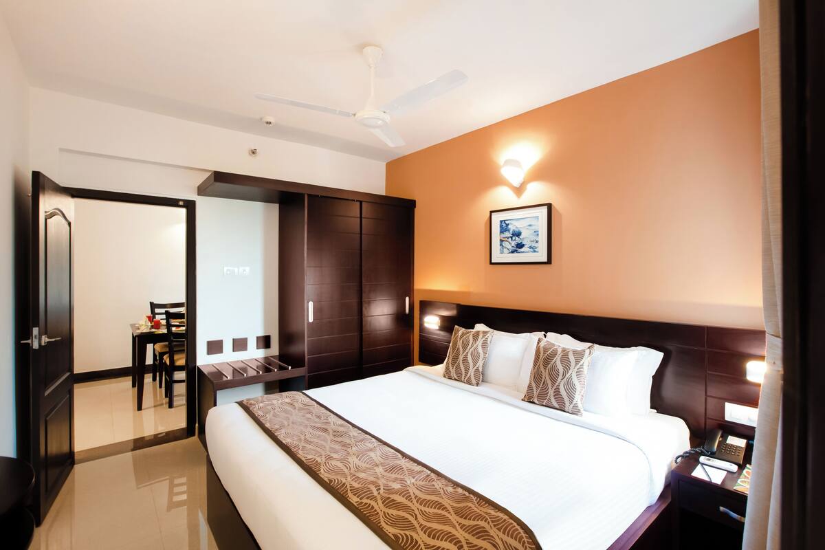 Une chambre d’hôtel avec un grand lit, un bureau, une chaise, une armoire et un ventilateur de plafond.