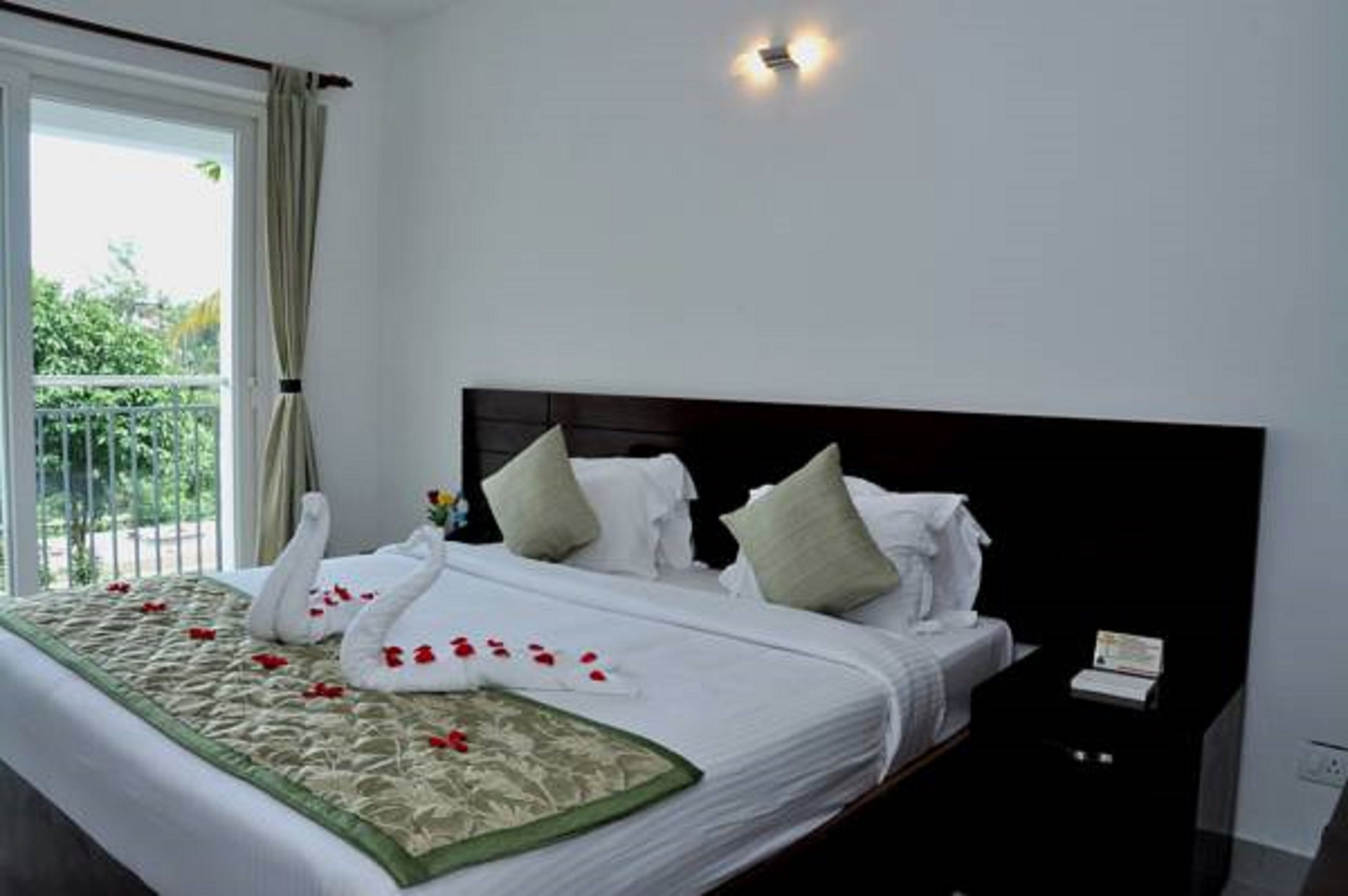 A hotel room with a large bed, a black headboard, and a view of greenery outside.