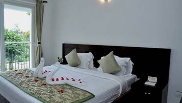A hotel room with a large bed, a black headboard, and a view of greenery outside.