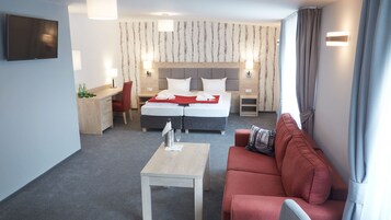 Quarto de hotel com cama, escrivaninha, sofá vermelho e televisão.