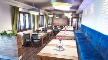Um restaurante com mesas de madeira, bancos estofados em azul e luminárias pendentes.