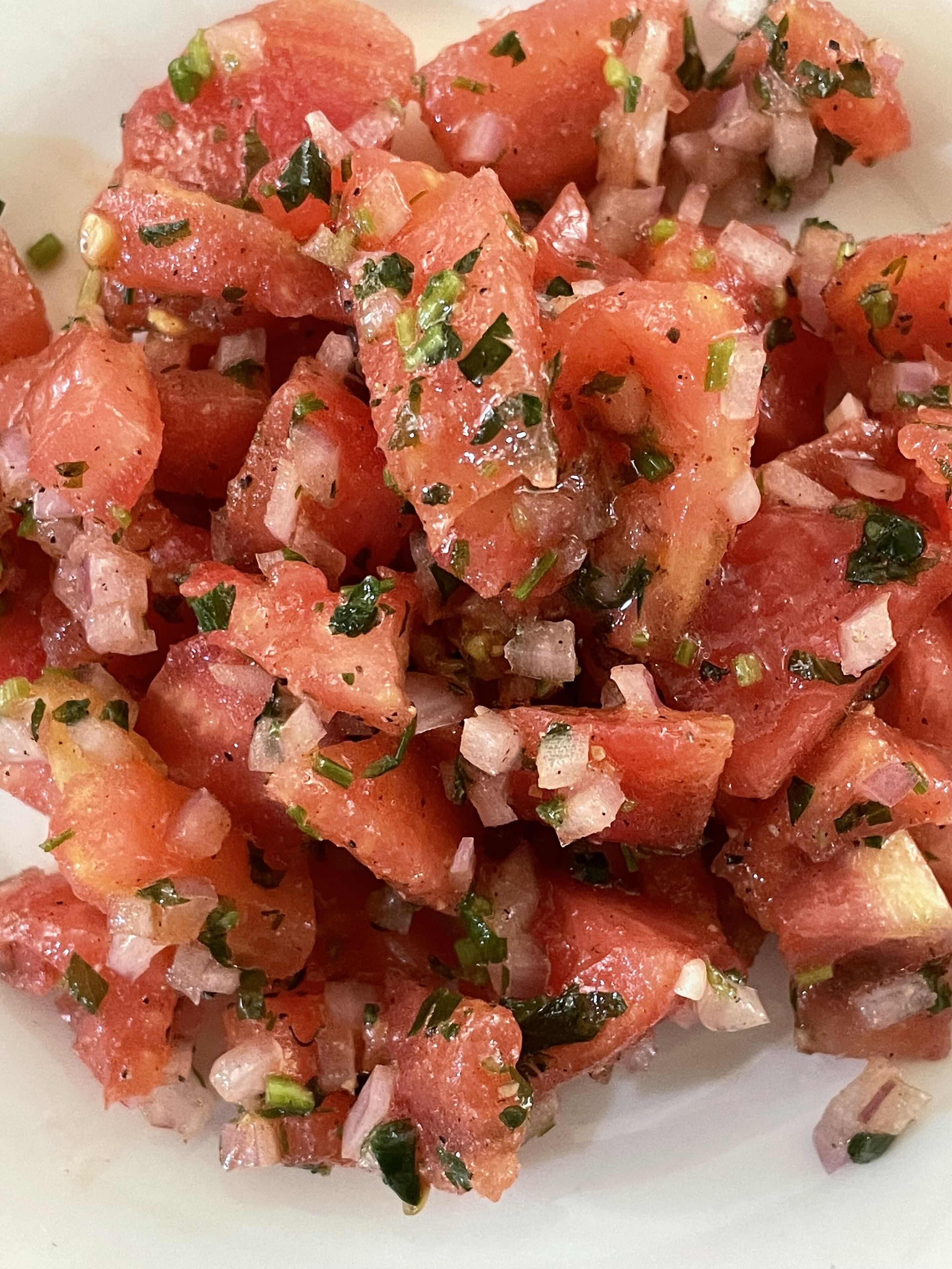 Primer plano de tomates en cubos con hierbas picadas y cebollas.