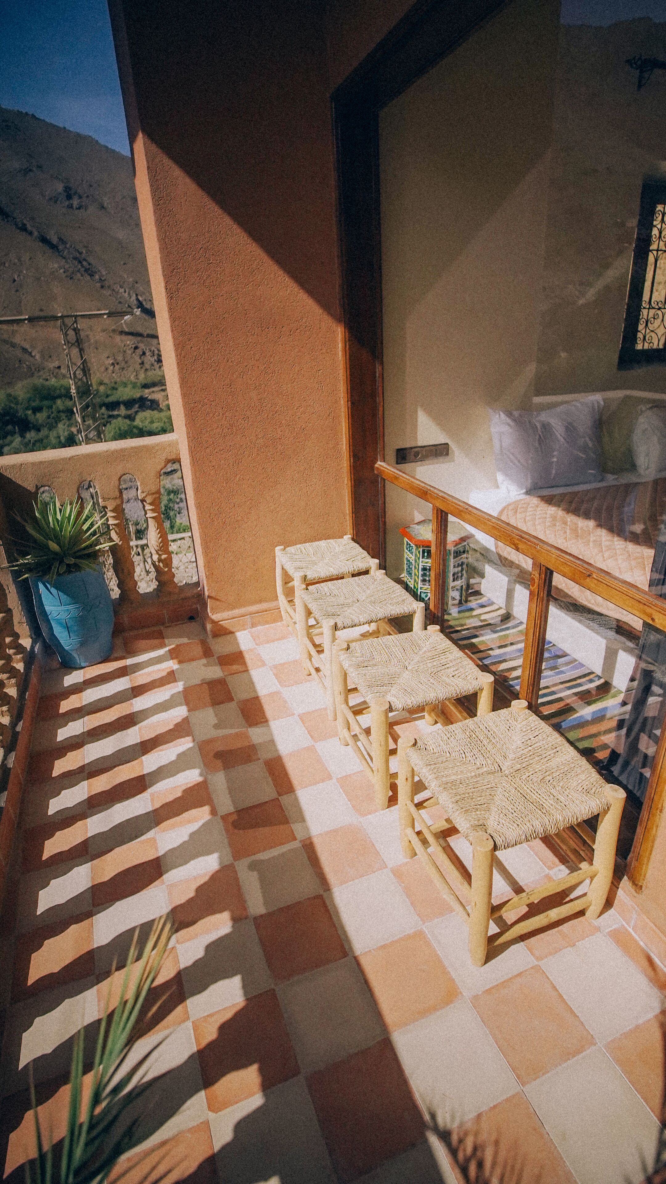 A balcony with checkered flooring, wicker furniture, a potted plant, and a view of a mountainous landscape.