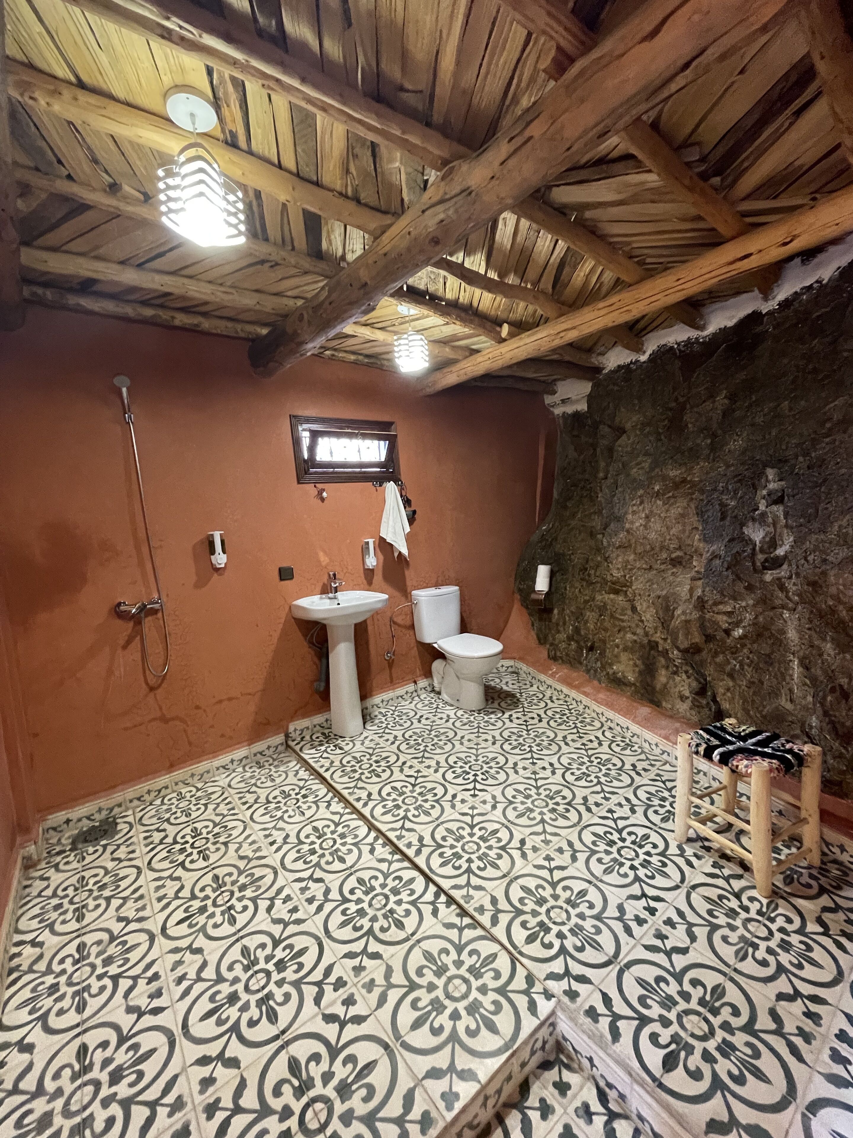 Un baño con techo de madera rústica, lavamanos, inodoro y ducha.