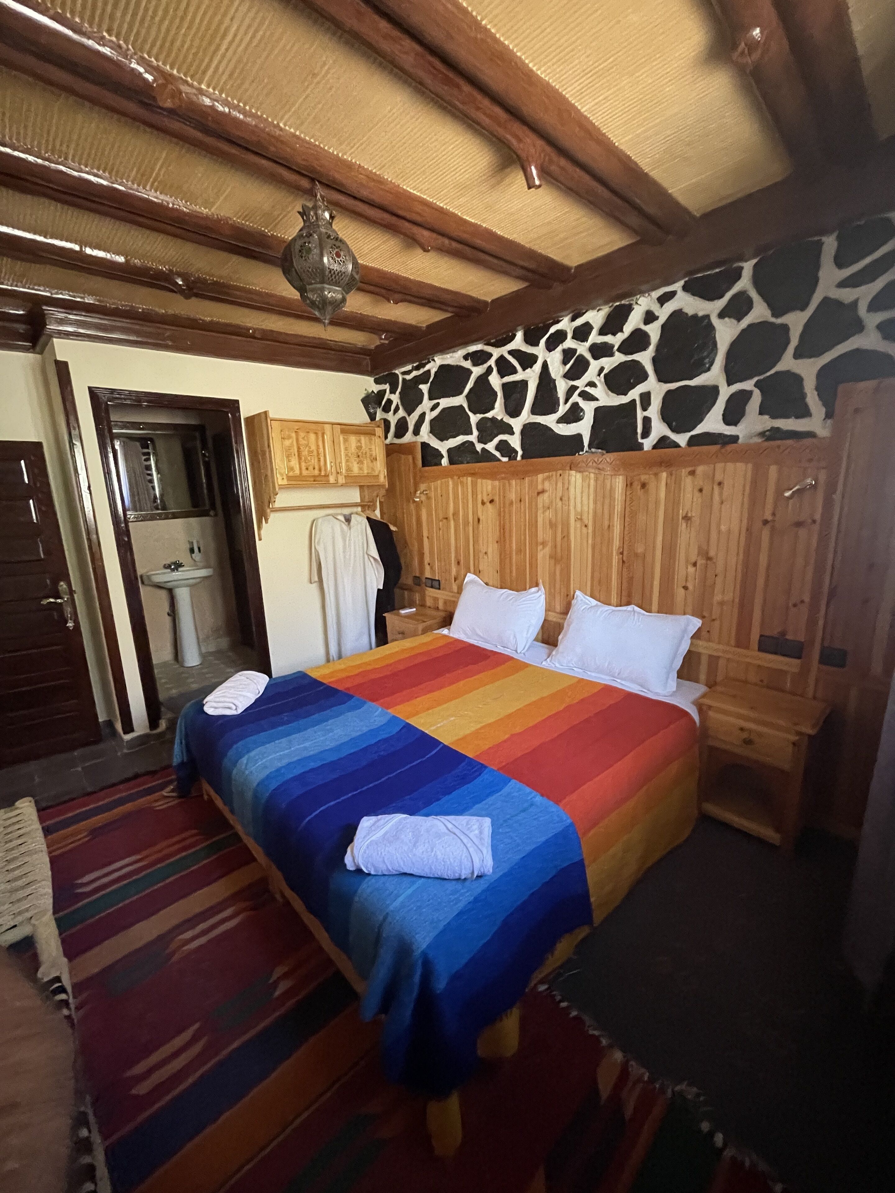 A bedroom with a bed, wooden headboard, and a stone wall.