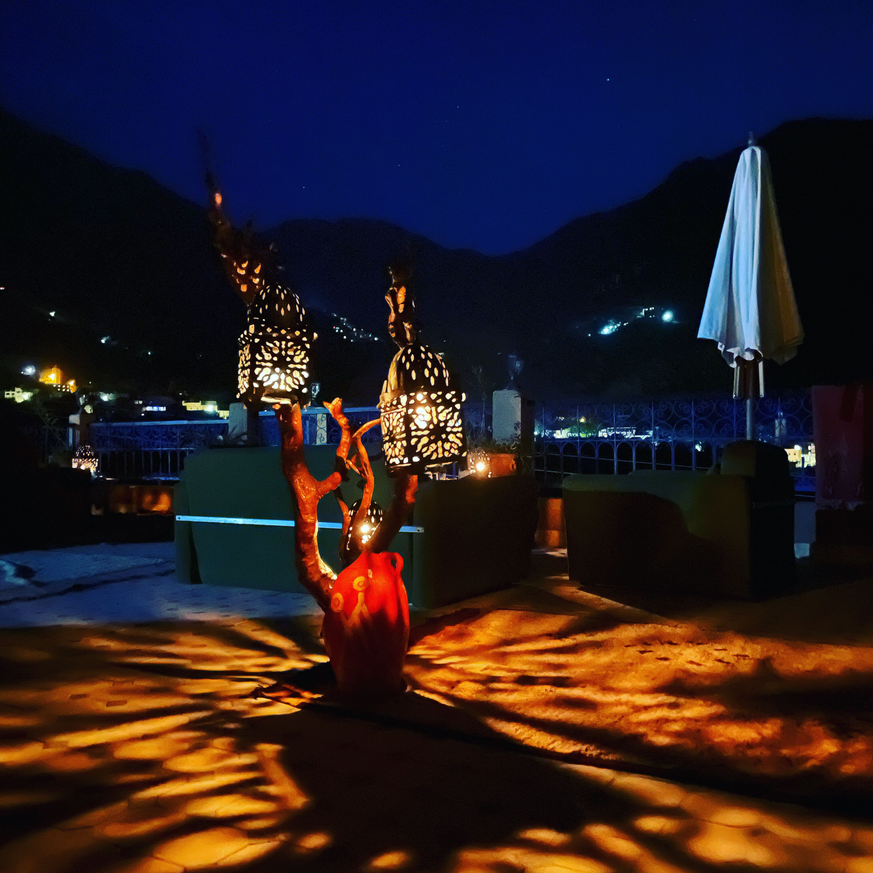 Una terraza en la azotea con iluminación decorativa y un jarrón rojo.