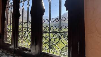 Un pasillo con tres ventanales de arco adornados con reja de hierro, que da a un paisaje montañoso.