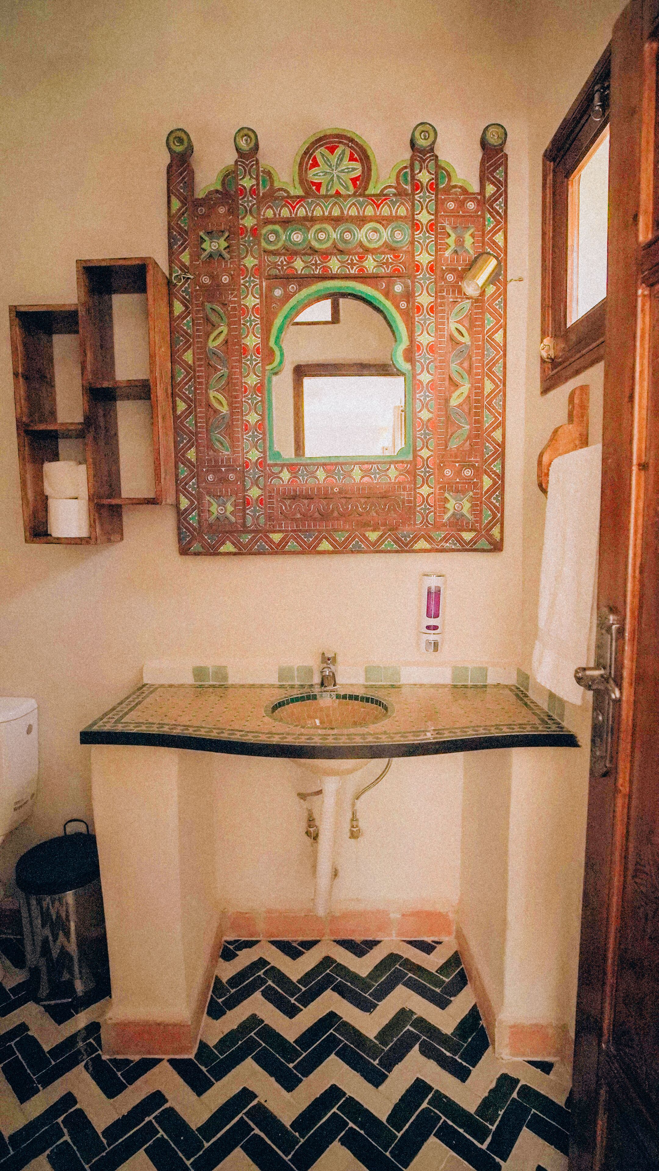 A bathroom with a patterned tile floor, a sink with a mirror above it, and a towel rack.