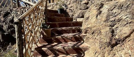 Unos escalones de piedra con barandilla de madera que ascienden por una ladera rocosa.