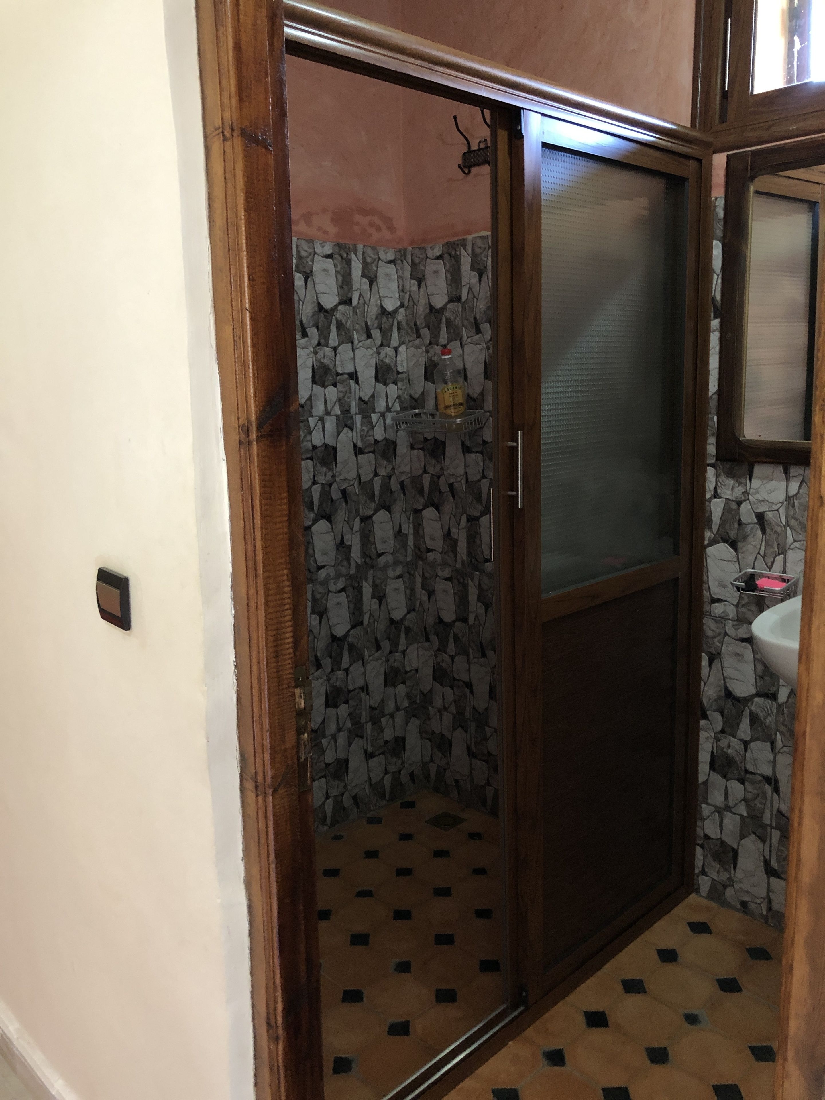 A bathroom with a stone wall, a tiled floor, and a wooden door.