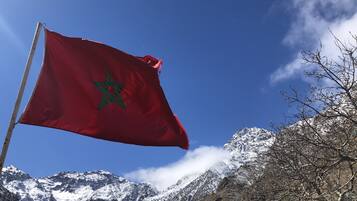 A red flag with a green star, set against a backdrop of snow-capped mountains and a clear blue sky.