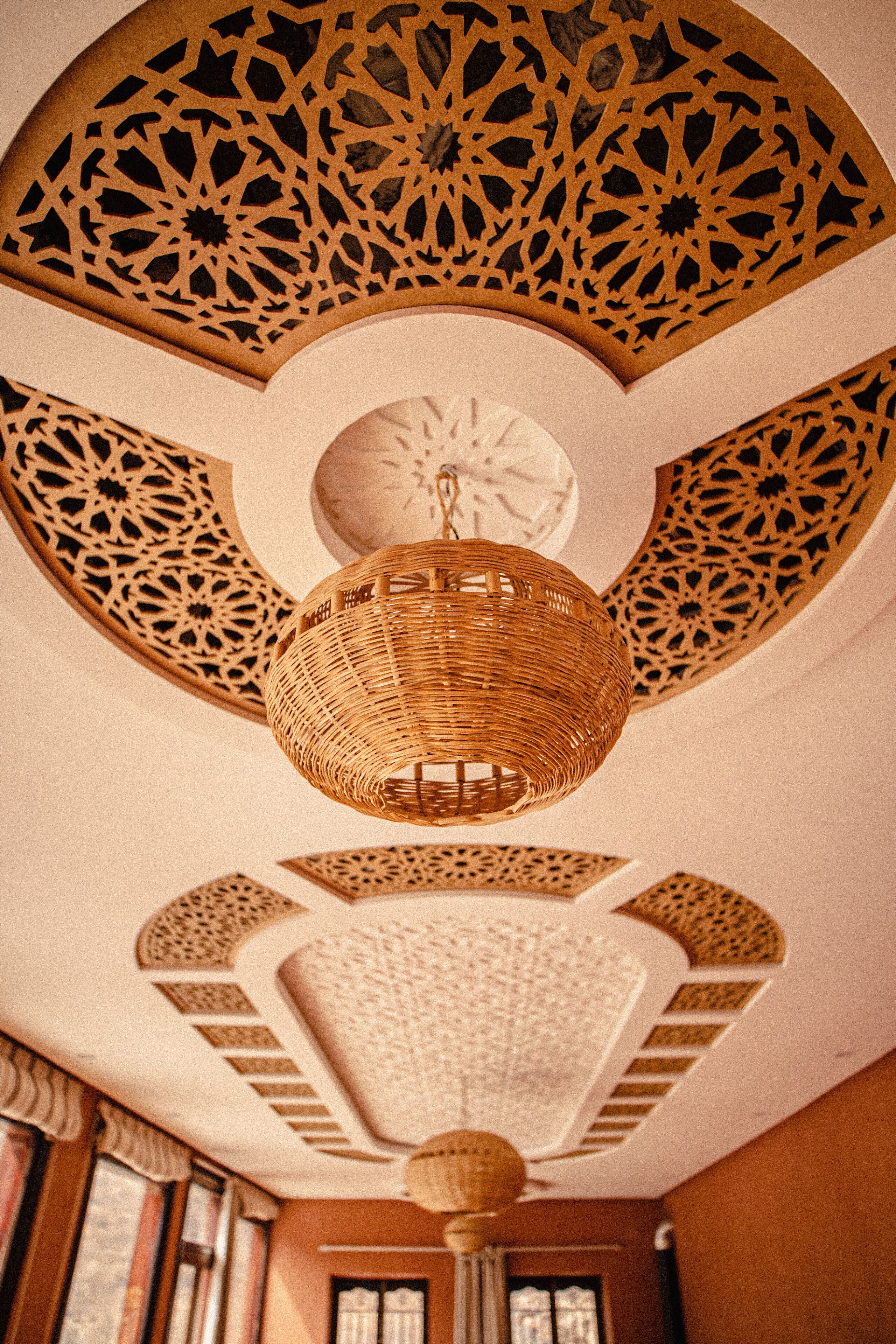 A room with intricate ceiling patterns, a central woven light fixture, and a circular skylight.
