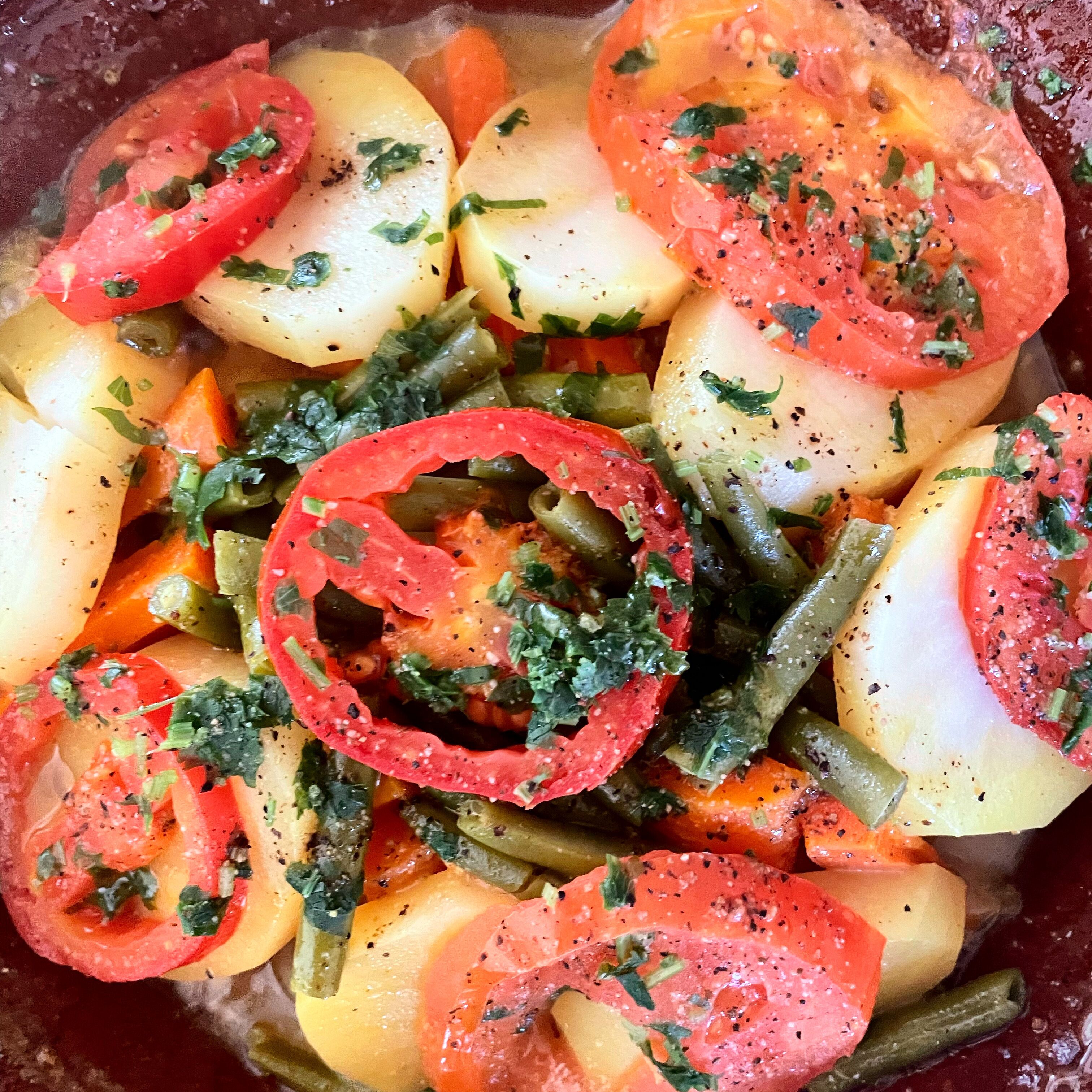 Primer plano de un plato de verduras con tomates en rodajas, judías verdes y patatas.
