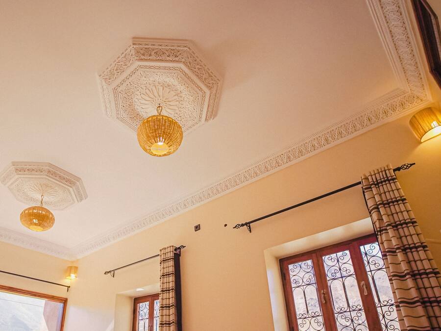 Una habitación con detalles ornamentales en el techo, un ventanal con vistas y una cortina de estampado a rayas.