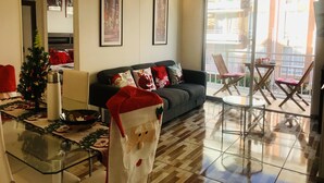 Una sala de estar con un sofá, decoraciones navideñas, una mesa de vidrio y un balcón con sillas.