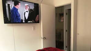 Un dormitorio con una cama estampada con un diseño de rosas, un televisor montado en la pared y una puerta que da a otra habitación.
