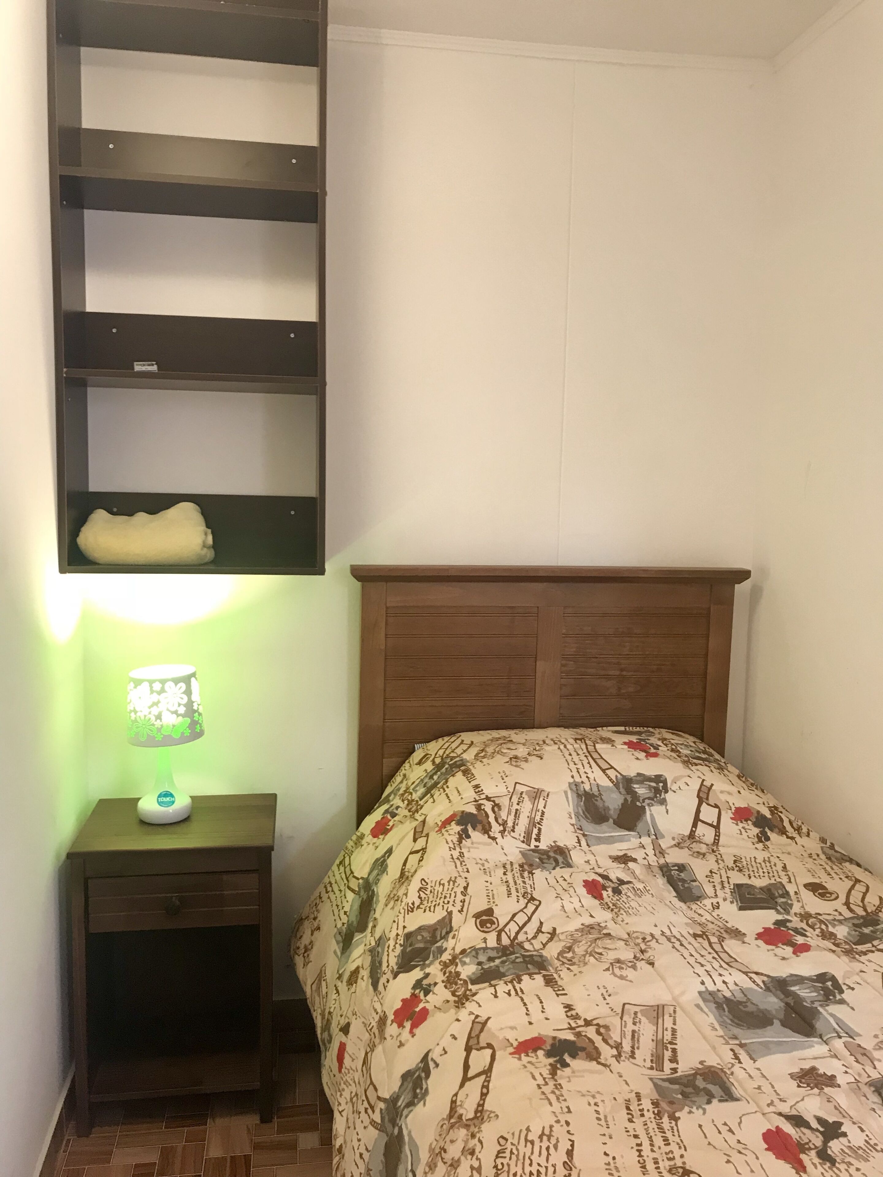 Un dormitorio con cabecera de madera, mesita de noche con lámpara y cama con colcha estampada.