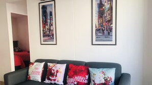 Una sala de estar con un sofá negro, cuatro cojines con motivos navideños y dos cuadros con vistas urbanas en la pared.