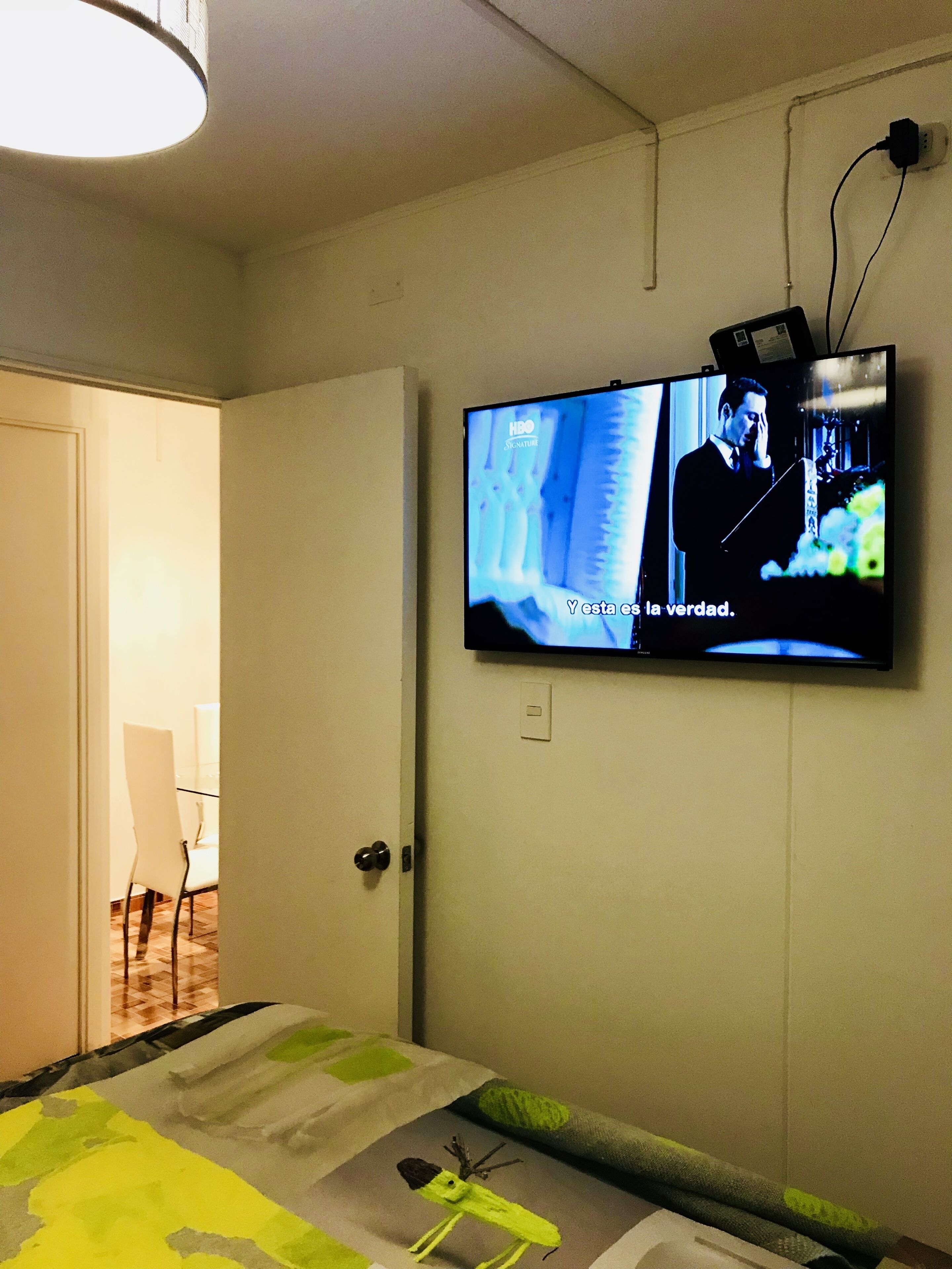 Una habitación de hotel con una cama, un televisor en la pared y una puerta que da a un comedor.