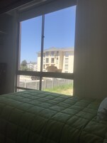 Una habitación con un ventanal grande, una cama verde y vistas a un edificio de enfrente.