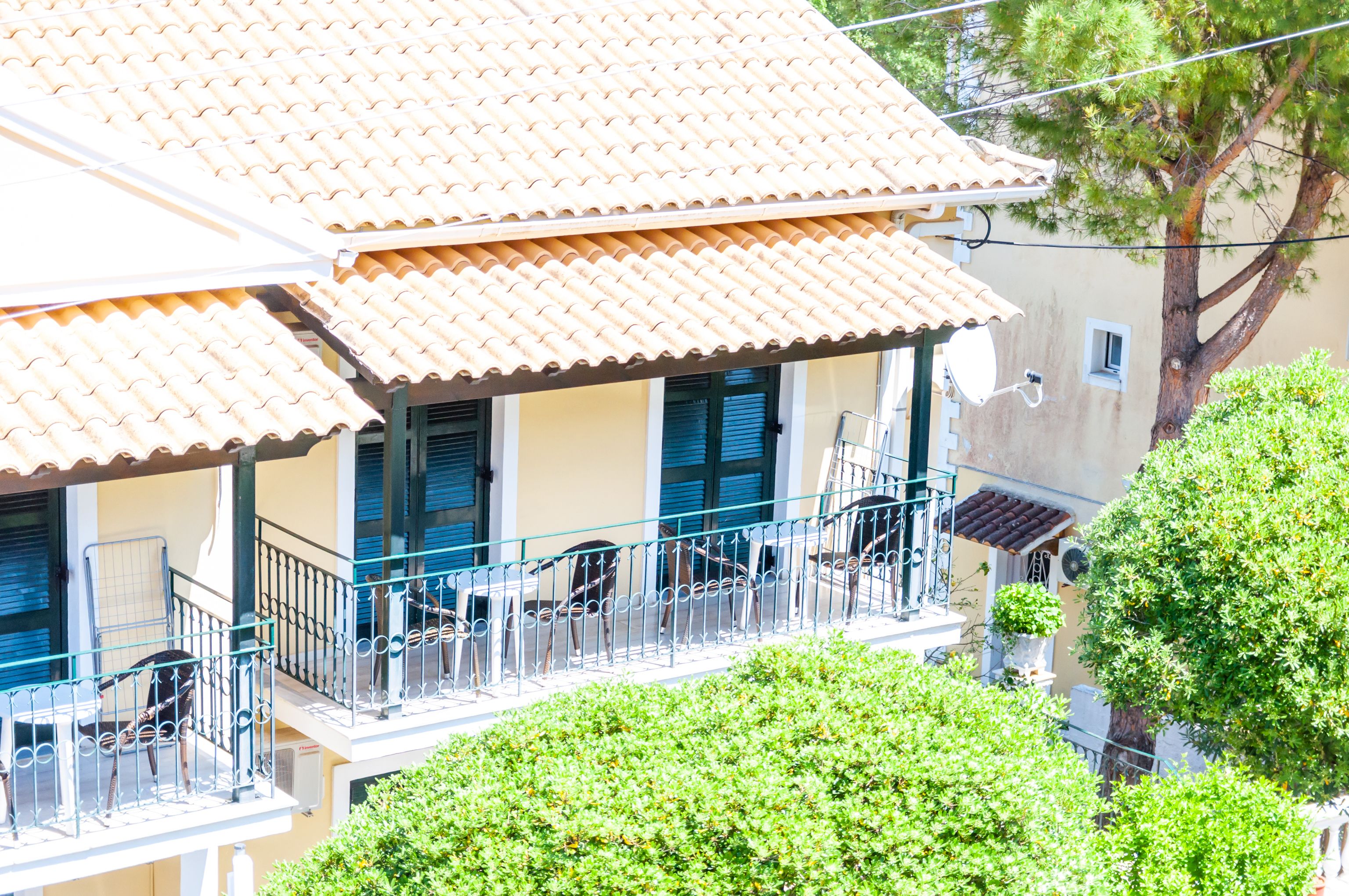 A building with a tiled roof, balconies with railings, and a tree in the background.