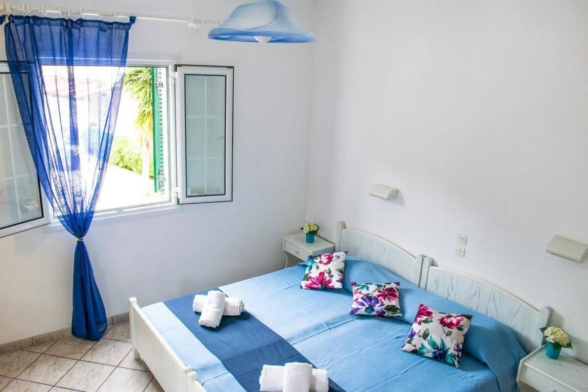 A bedroom with a bed, blue curtains, a window, and a nightstand with a lamp.