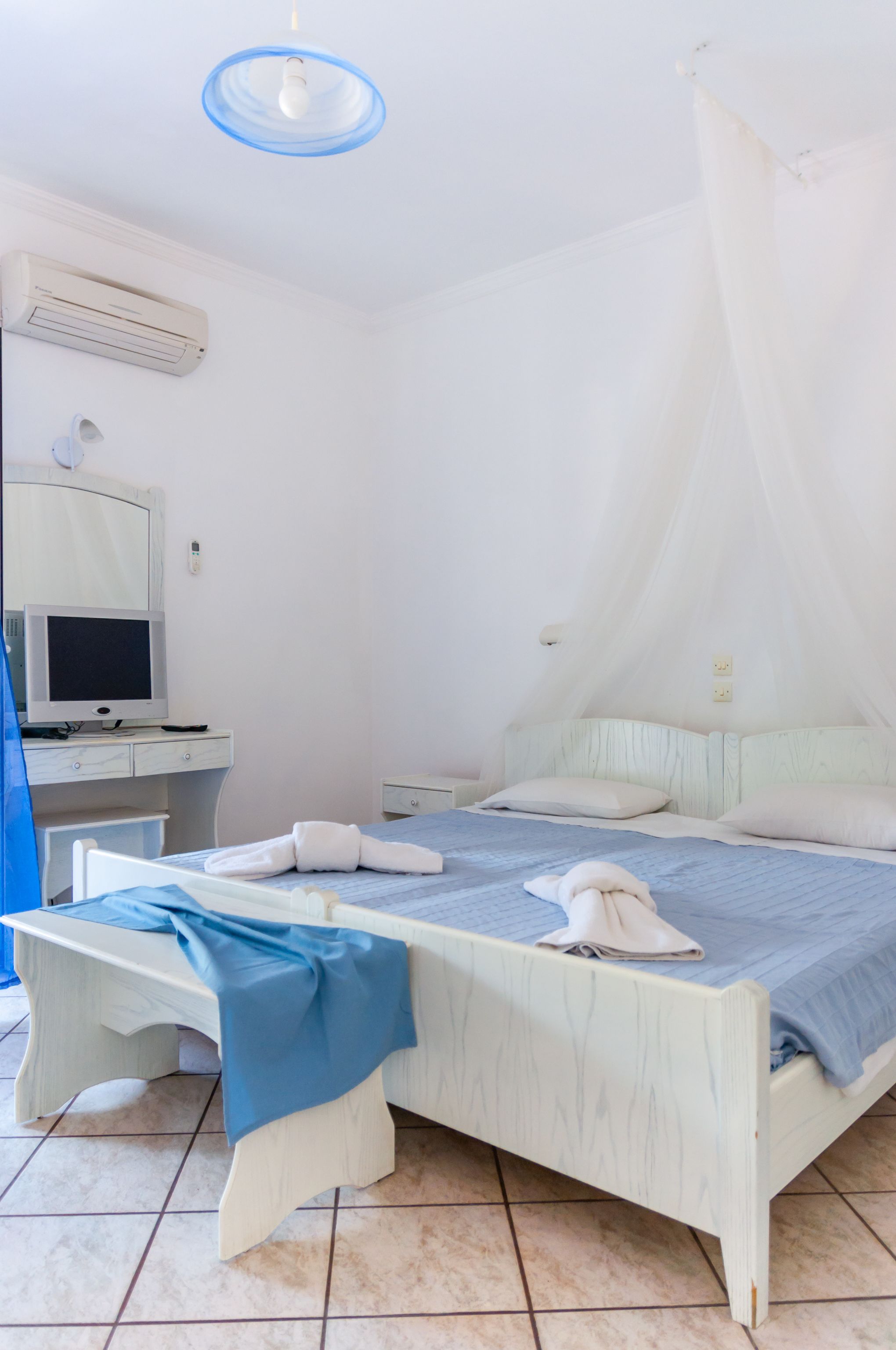 A bedroom with a bed, bedside table, and a television on a desk.