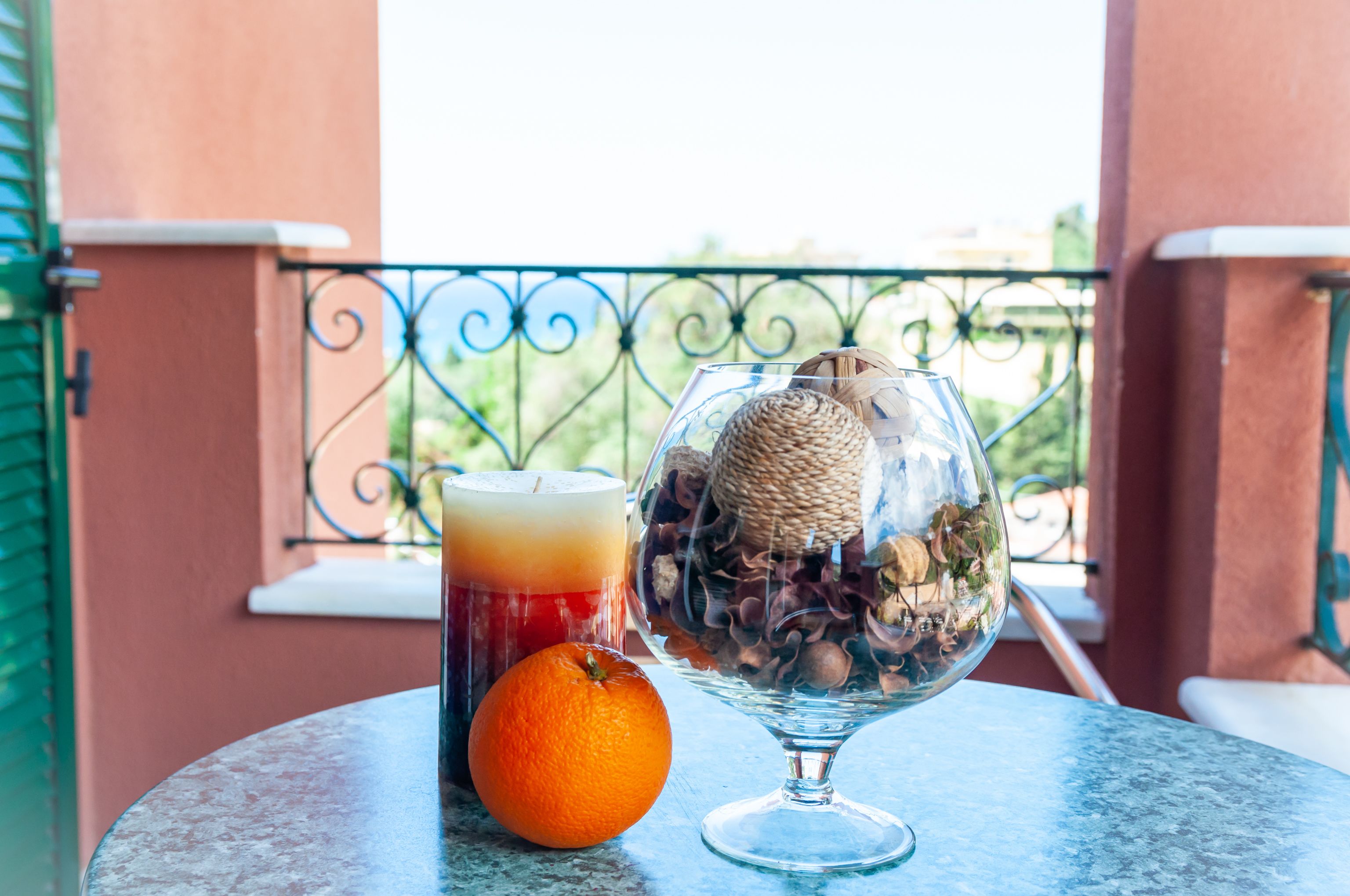 Un tavolo con un bicchiere di succo, una candela e un'arancia su un balcone.