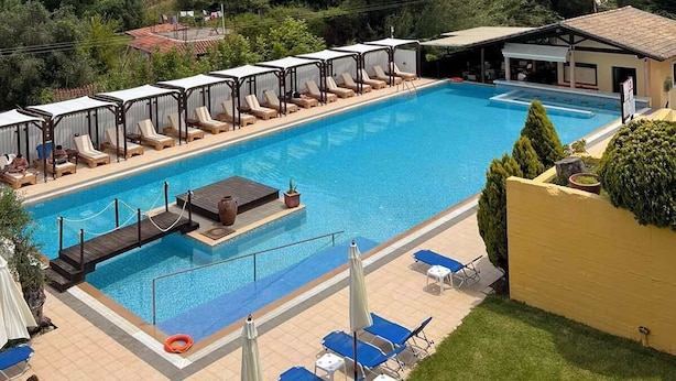 Una piscina con sillas de descanso y sombrillas, rodeada de abundante vegetación y colinas.