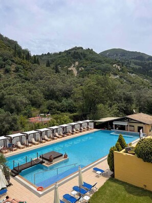 A swimming pool with lounge chairs and umbrellas, surrounded by lush greenery and hills. - Apart Hotel Blumarin (Corfu)