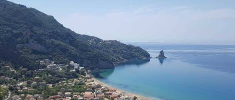 Un pueblo costero con playa, casas y una imponente formación rocosa en el mar.