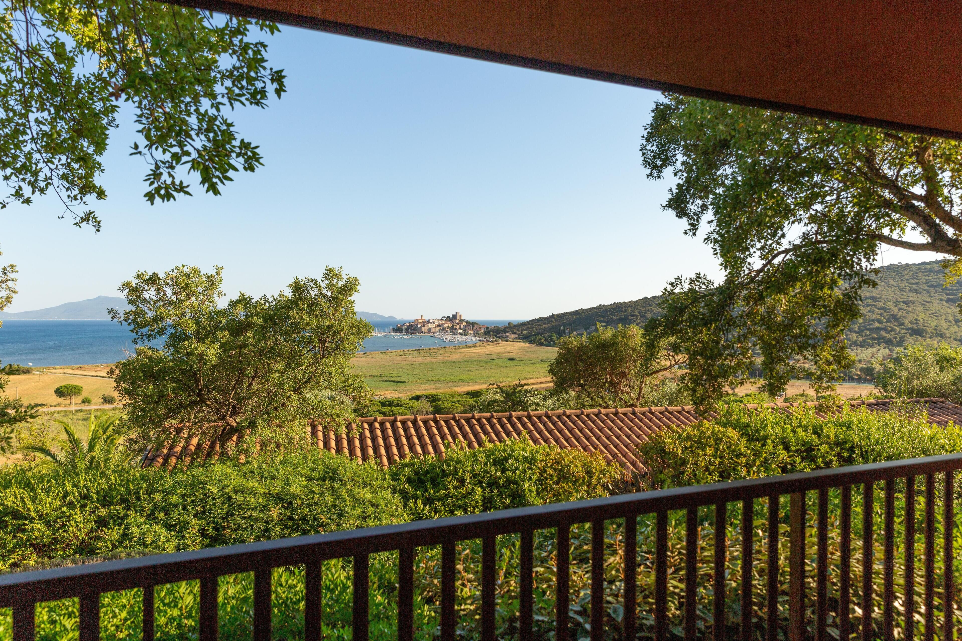 A terrace with a view of a vineyard, a distant body of water, and hills.
