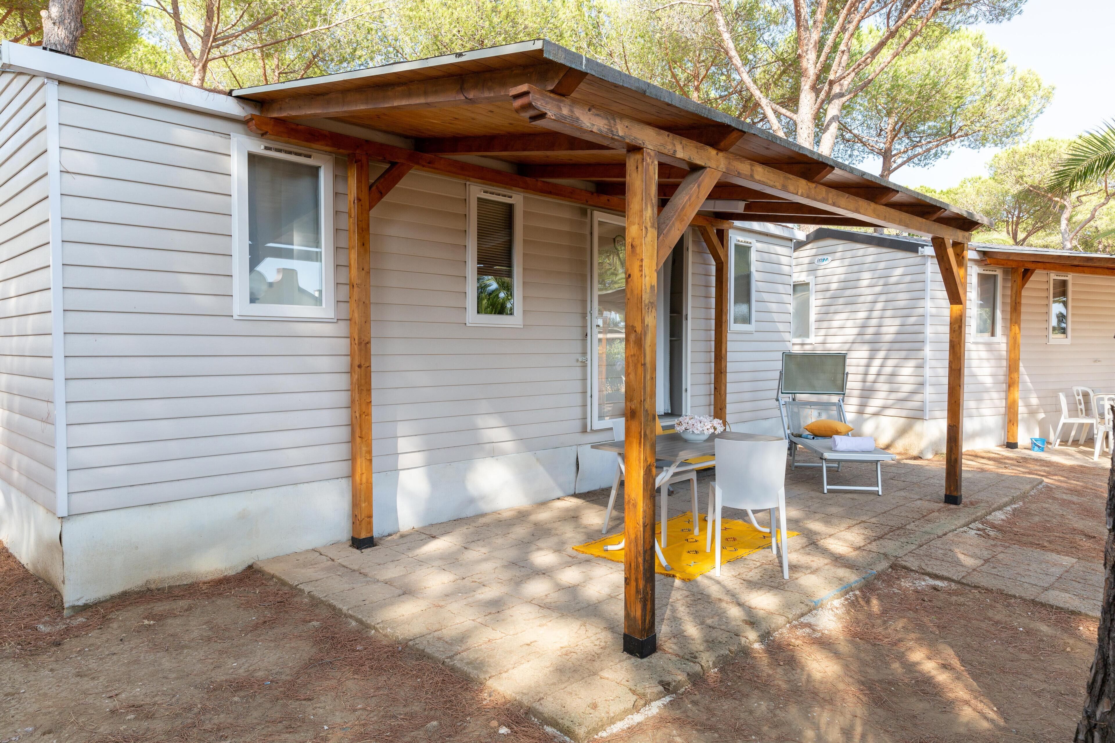 Une maison mobile dotée d’un porche en bois, d’un espace salon extérieur et d’un petit patio.