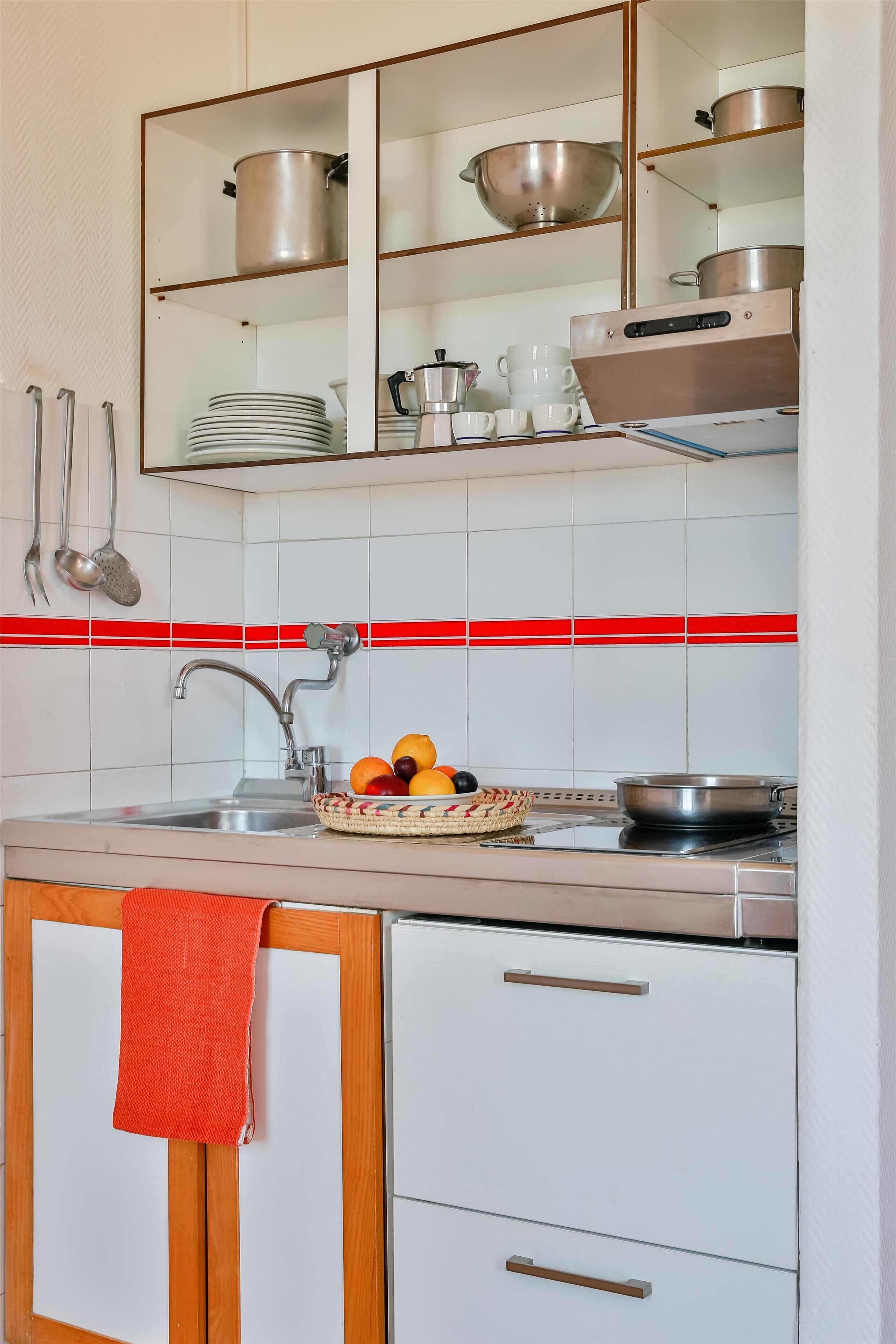 Una cocina con armarios blancos, un lavamanos de acero inoxidable y un salpicadero a rayas rojas.